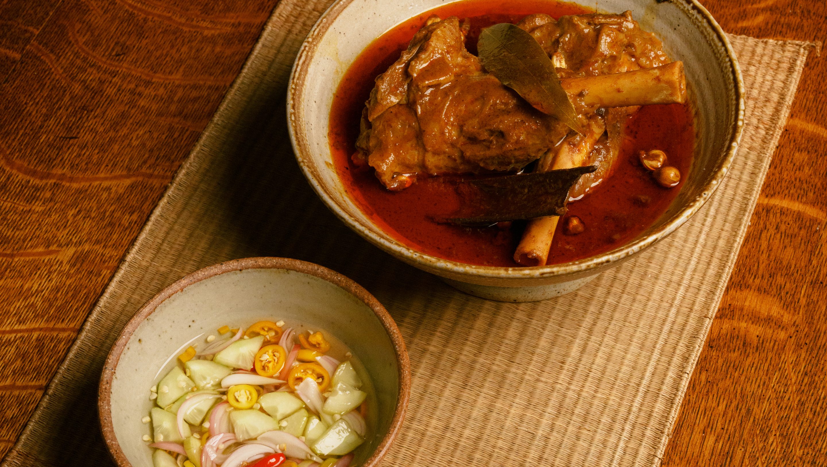A slow-cooked curry beside a bowl of cucumber relish on a woven placemat